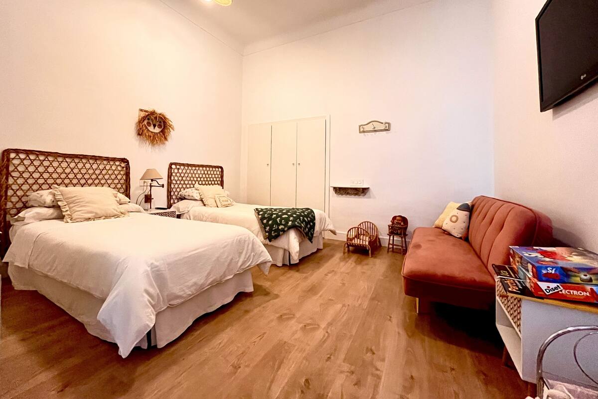 Une chambre avec deux lits, un canapé rouge, une télévision et une petite table sur laquelle se trouvent divers objets.