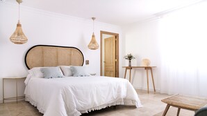 Un dormitorio con una cama grande, dos mesitas de noche, una puerta de madera y una pequeña mesa con una planta.