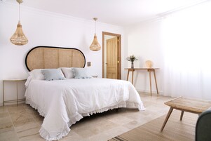 A bedroom with a large bed, two bedside tables, a wooden door, and a small table with a plant.