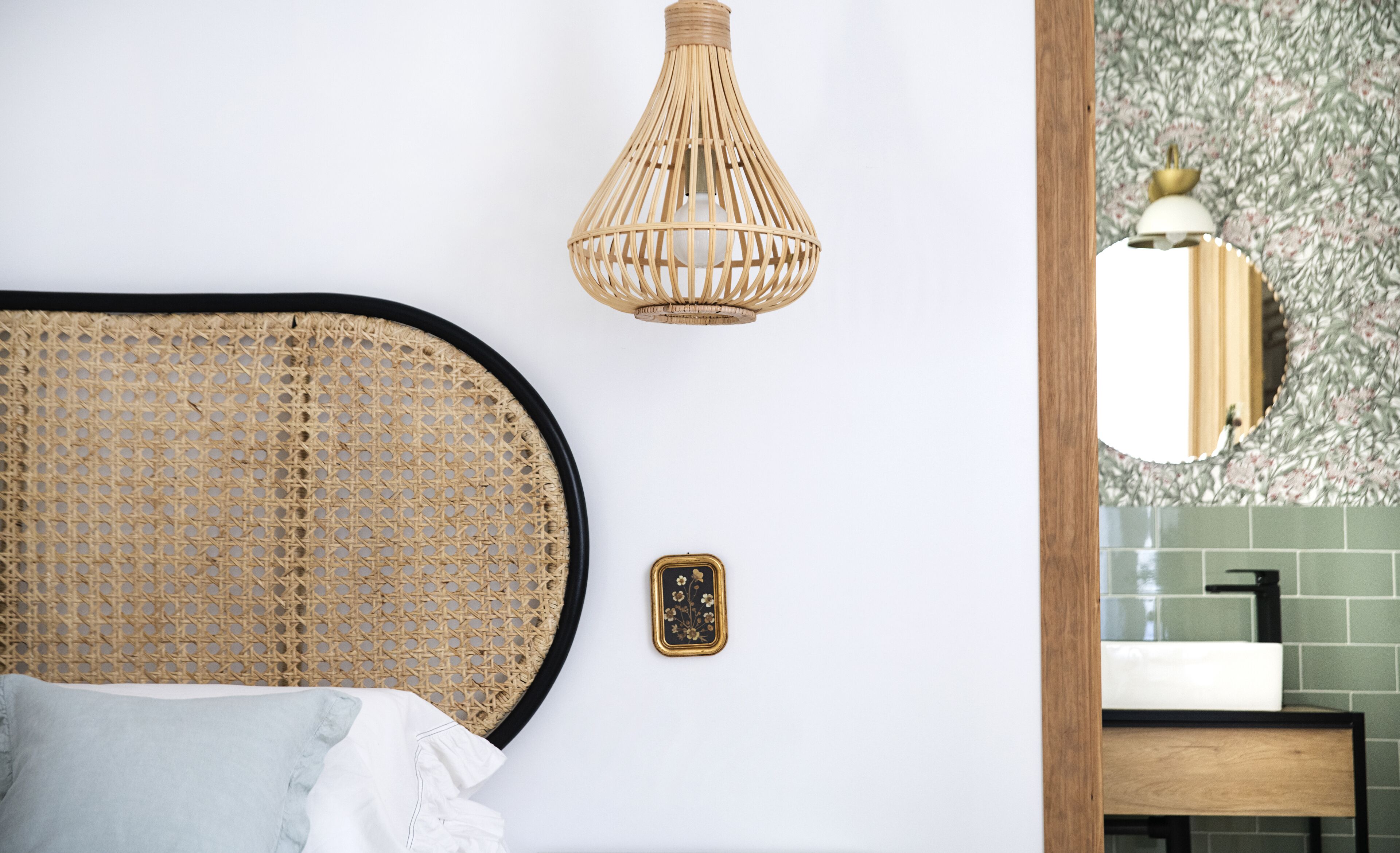 A bathroom with a woven headboard, a wall-mounted light fixture, a small decorative plate, and a mirror with a floral pattern.