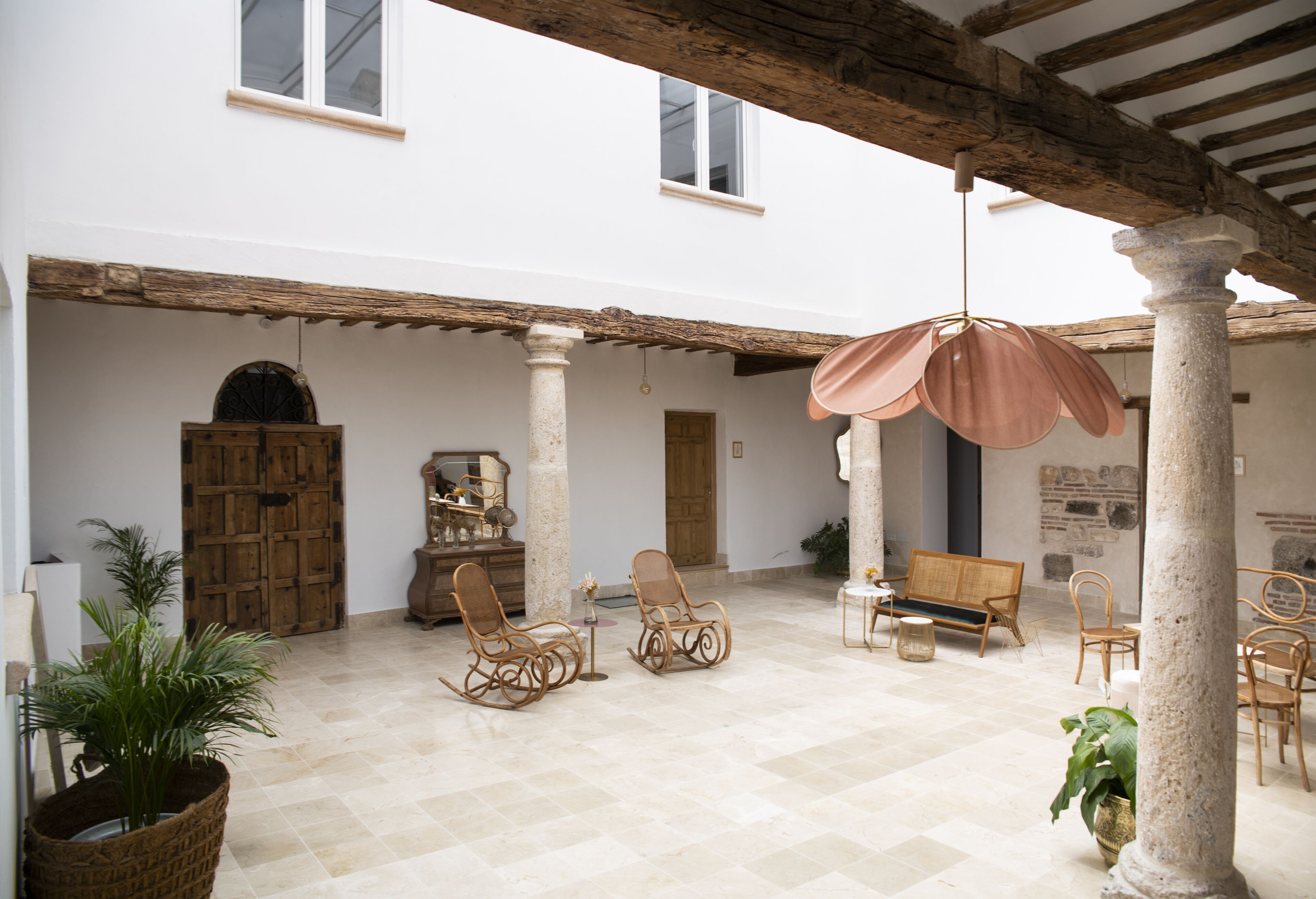 A spacious courtyard with a wooden pergola, wicker furniture, and a hanging light fixture.