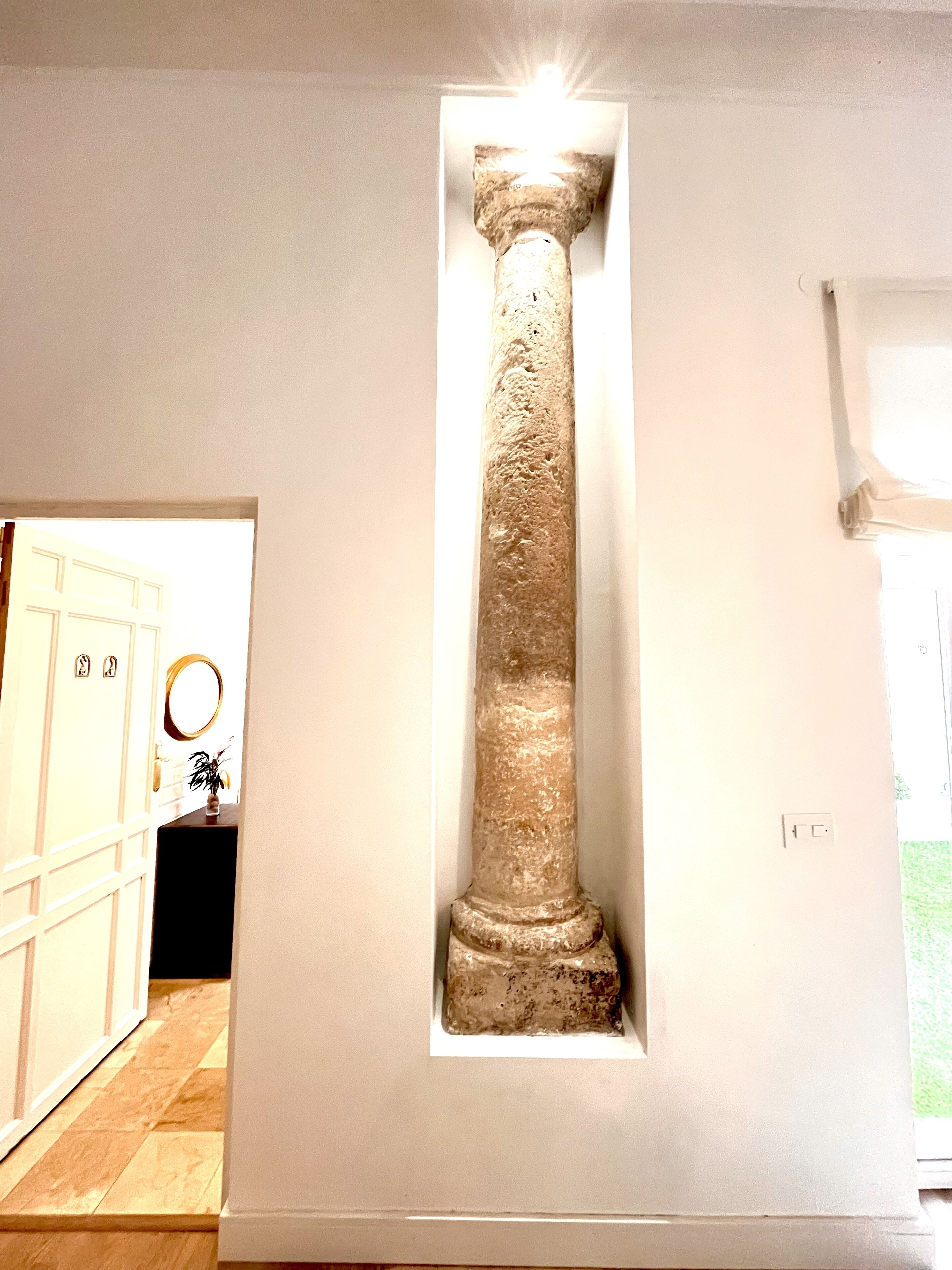 A room with a large, illuminated pillar, a door with a mirror, and a small plant on a dark surface.