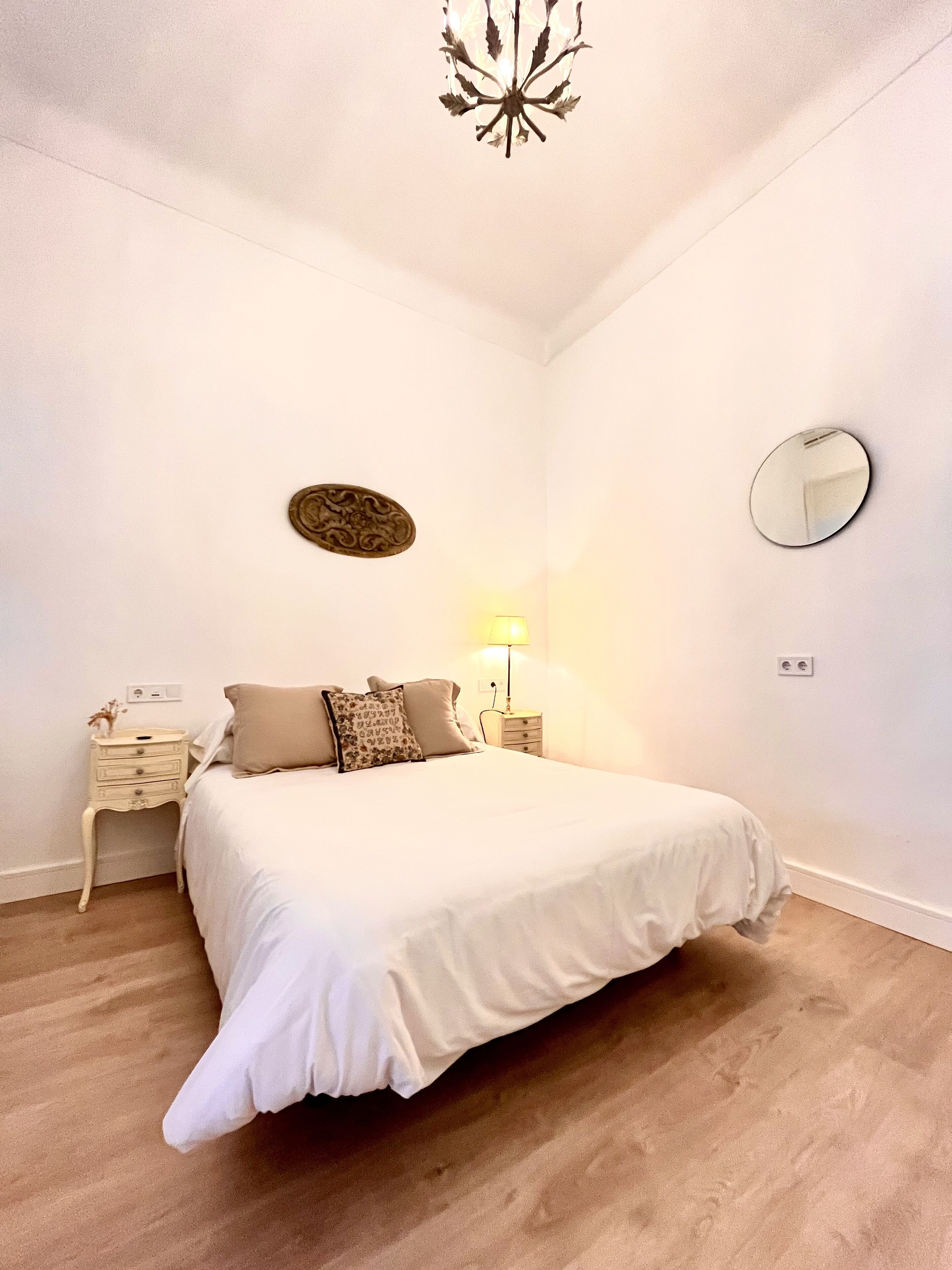 A bedroom with a bed, nightstands, a lamp, a mirror, and a decorative wall piece.