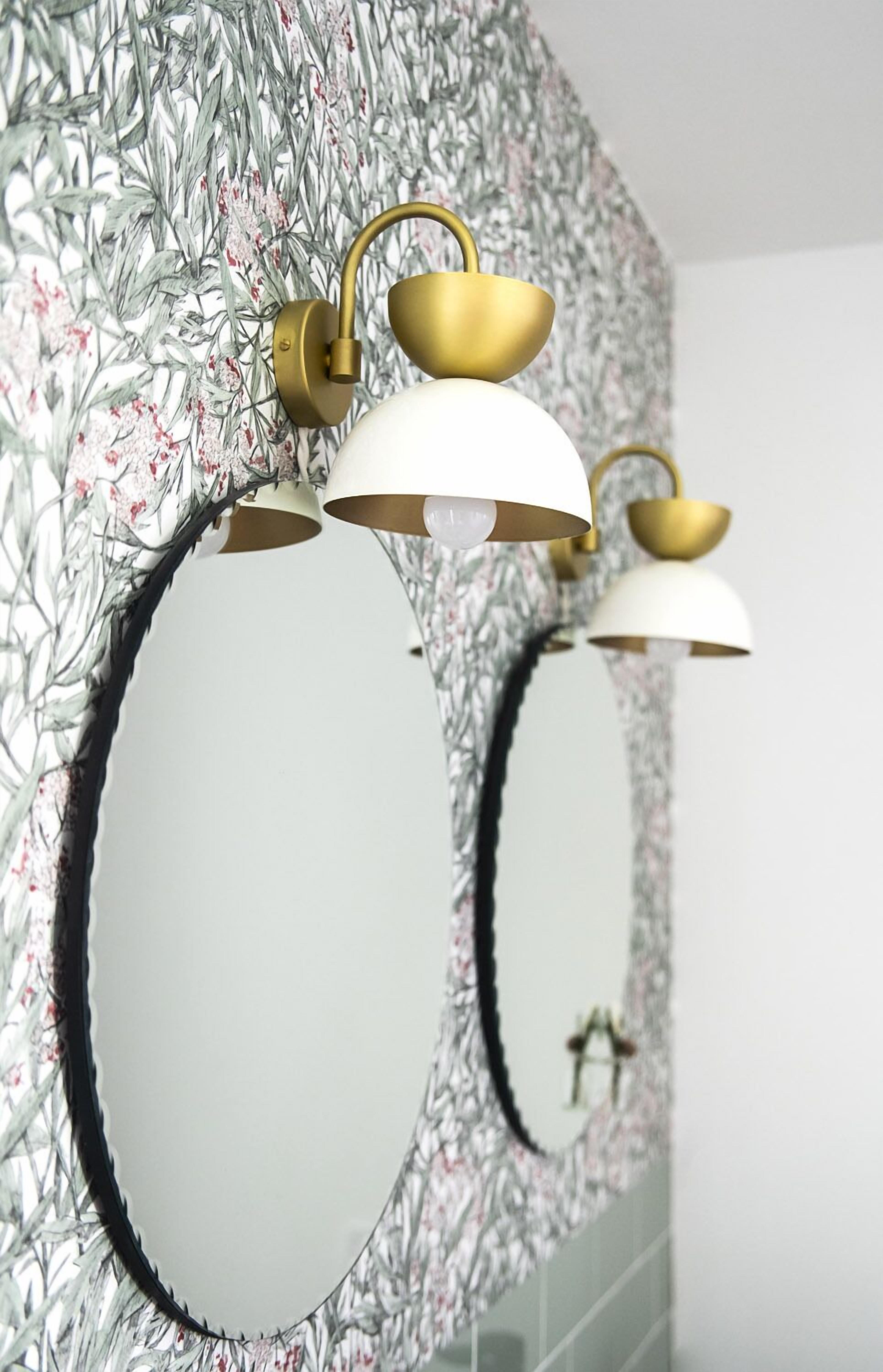 Un baño con un espejo grande, una lámpara de pared y un diseño de papel tapiz floral.