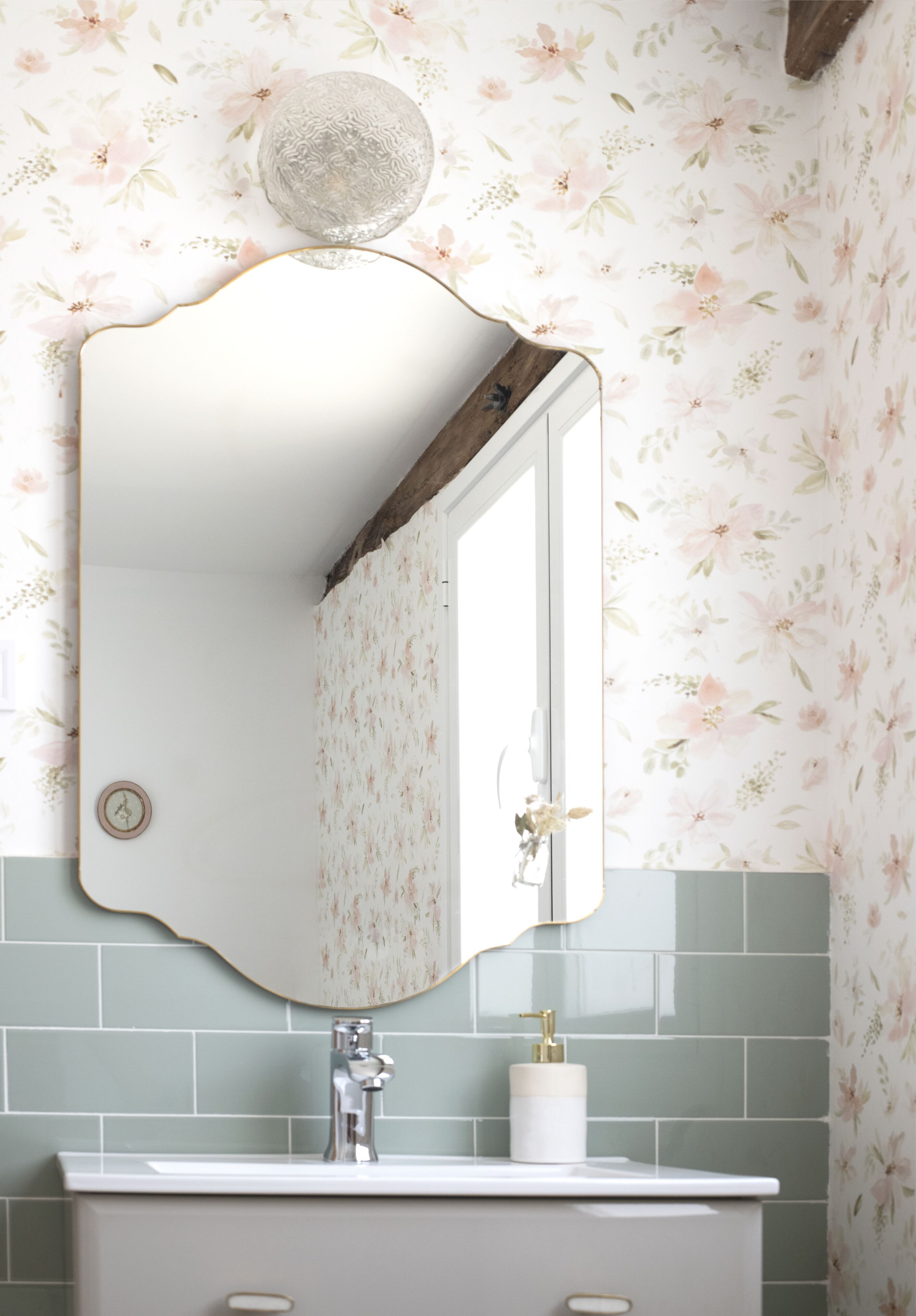 A bathroom with floral wallpaper, a round mirror, a white sink, and a green tiled backsplash.
