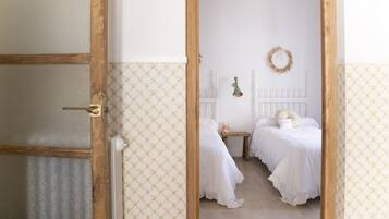 A room with two beds, a small table, a wall-mounted light, and a wreath on the wall.