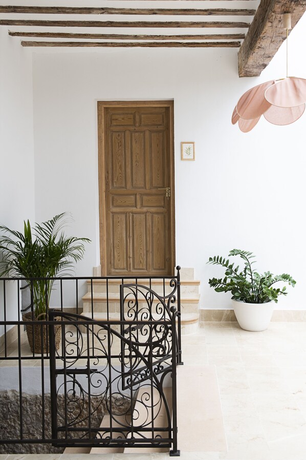 Una puerta de madera con una reja metálica decorativa, macetas con plantas y una escalera que sube a un nivel superior.