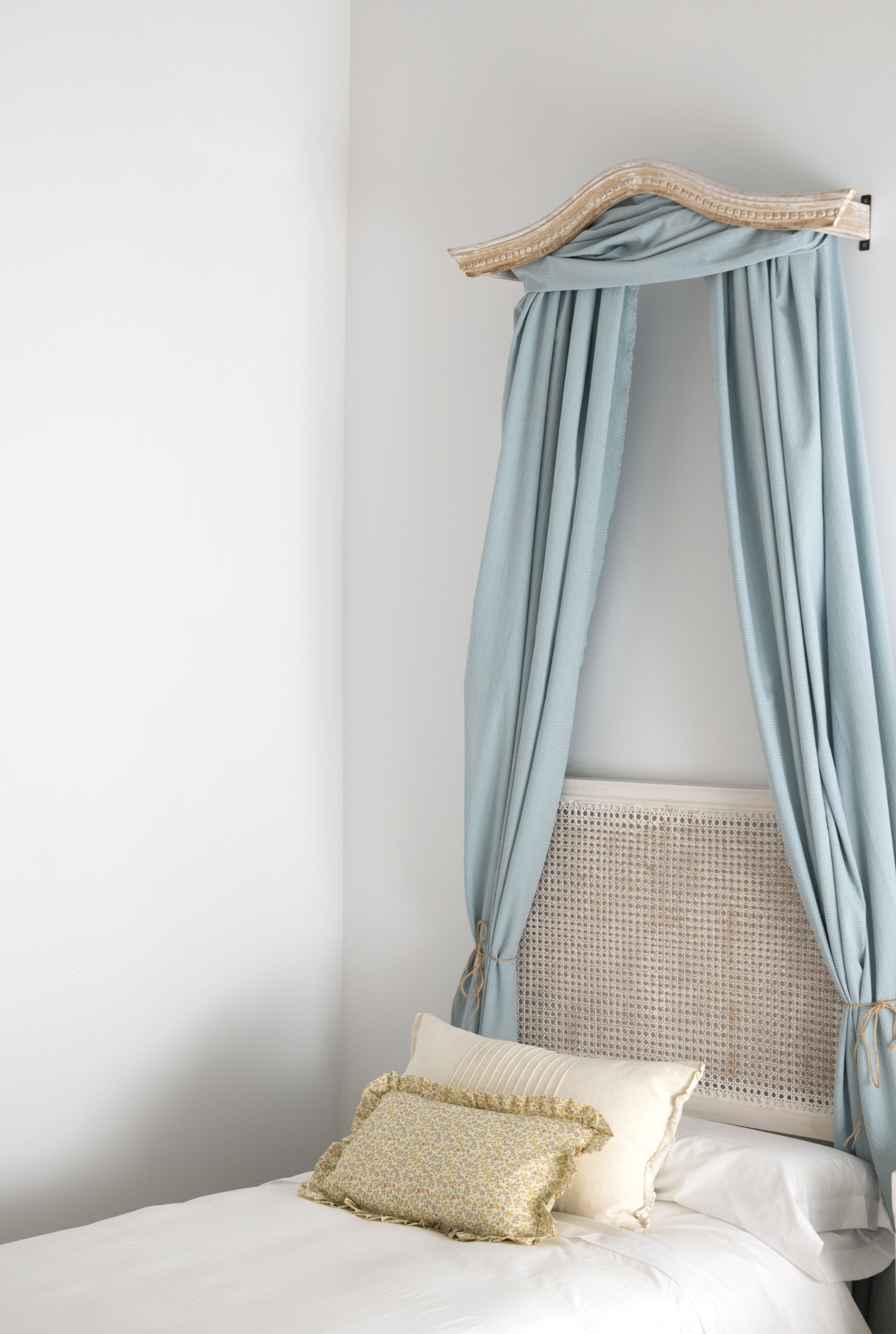 A bedroom with a canopy bed, a woven headboard, and two pillows.
