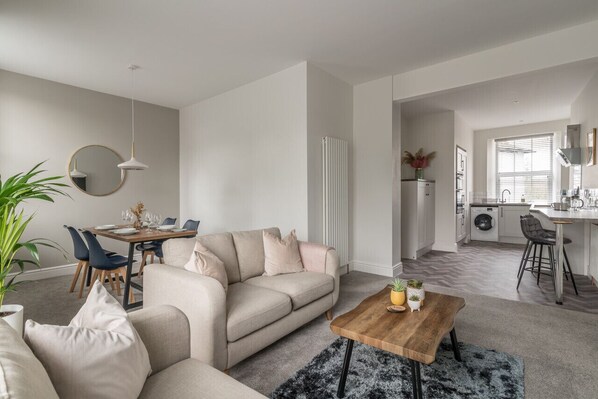 A modern living room with a beige sofa, a wooden coffee table, and a dining area with a round table and chairs.
