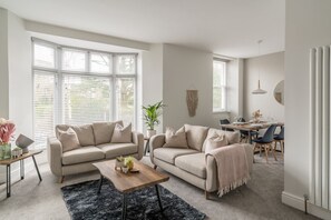 Un salon moderne avec deux canapés beige, une table basse en bois et un coin repas comprenant une table et des chaises.