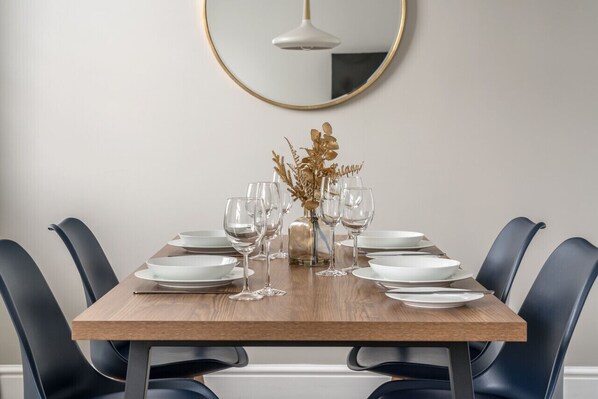 Une table à manger dressée avec de l’assiette blanche, des verres transparents et un vase contenant des fleurs séchées.