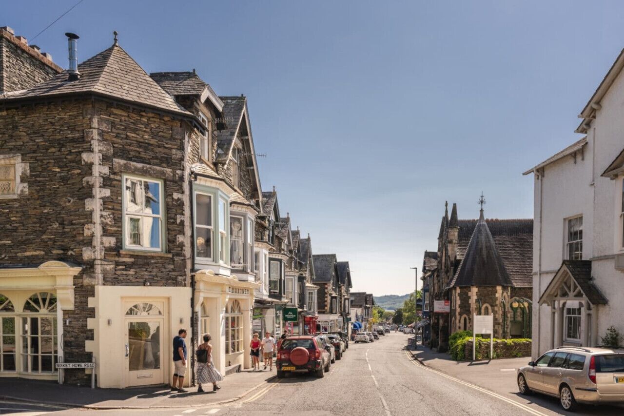 Eine Straße mit historischen Steinbauten, einem Schild für 'BISKEY HOW ROAD' und parkenden Autos.