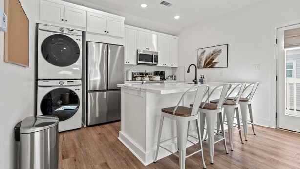 A modern kitchen with stainless steel appliances, a central island with bar stools, and white cabinetry. - Island Gems - Gold

 (Galveston)