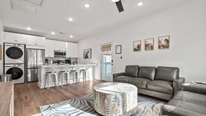 A modern kitchen with white cabinets, stainless steel appliances, and a bar area. There is a gray leather sofa and a patterned rug in the living area. - Island Gems - Gold

 (Galveston)