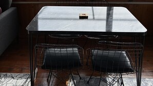 A room with a large window, a table with two chairs, and a view of a park and body of water.