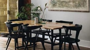 A dining area with a wooden table and black chairs, a brick wall, a globe light, and a forest painting. - Ulysses Suites, Suite 203 (Galena)