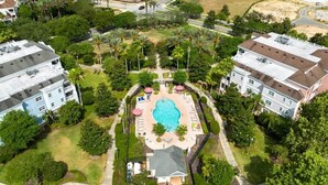 A residential area with a swimming pool, surrounded by greenery and adjacent to multi-story buildings. - GolfView Condo w/ $50 ThemePark Credit Near Disney (Reunion)