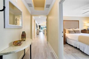 Een hotelgang die leidt naar een slaapkamer met een bed, nachtkastje, lamp en een spiegel aan de muur.