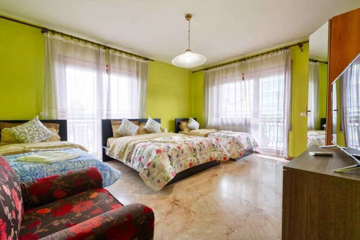 A room with two beds, a sofa, a desk, and a large window with curtains.