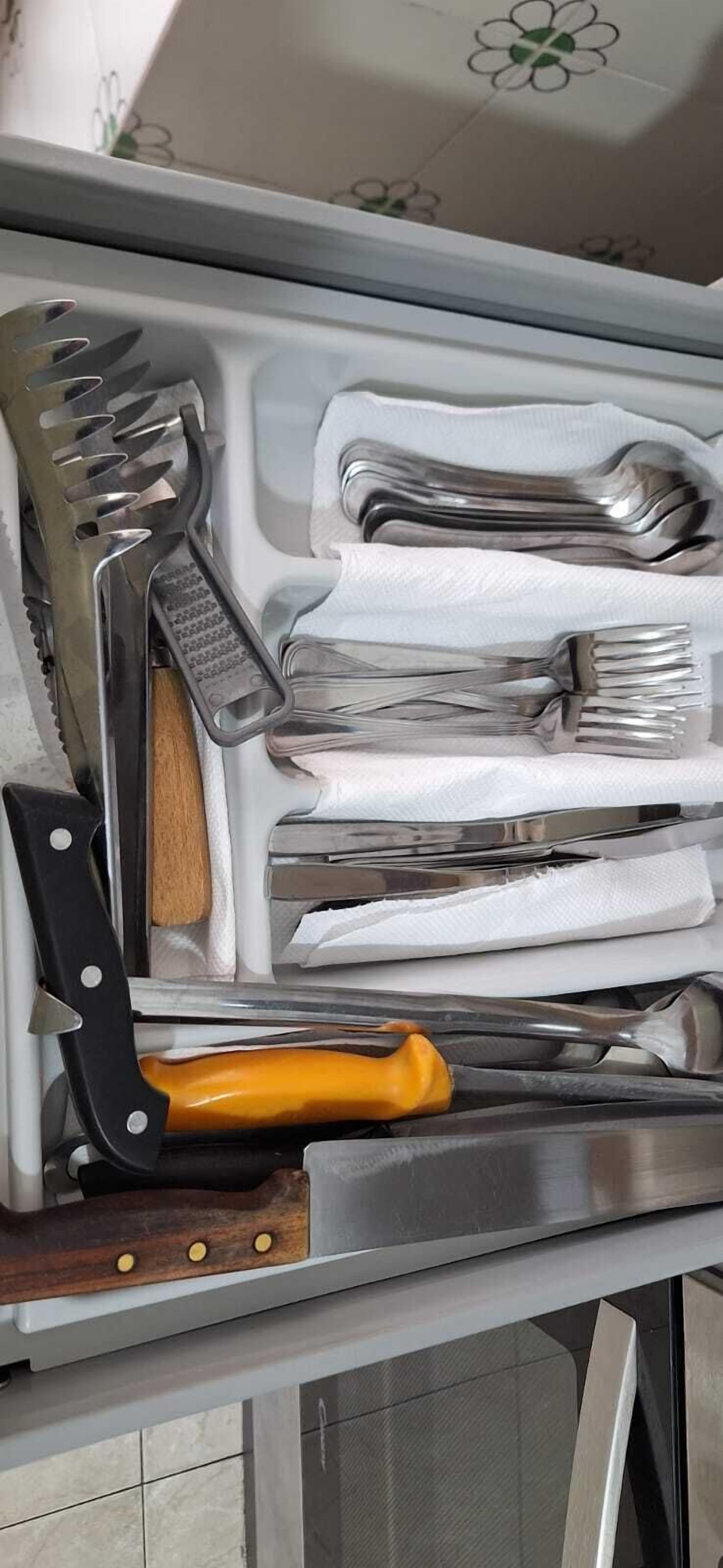 A drawer containing various kitchen utensils including a knife, fork, and spoon.