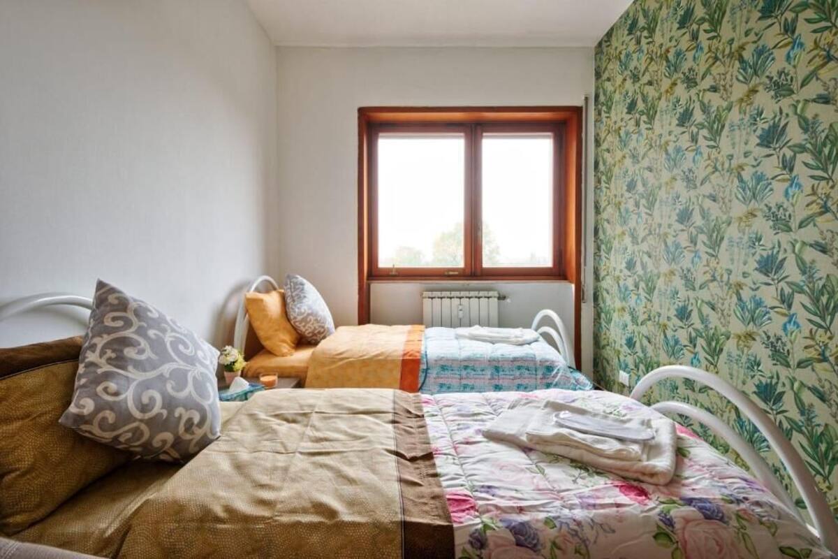 A bedroom with two beds, a radiator, and a window with a view.