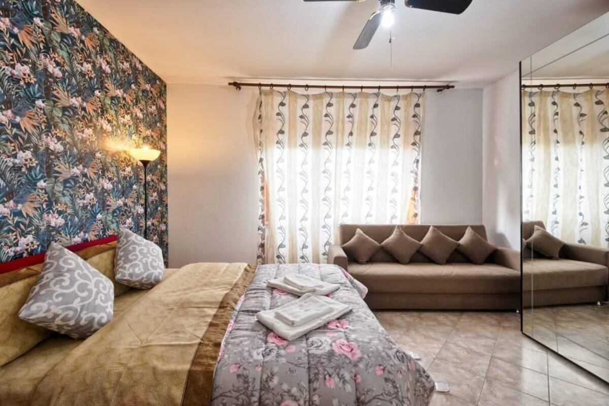 A bedroom with a bed, a sofa, a mirror, and curtains.