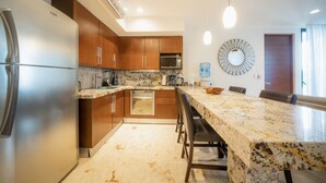 A modern kitchen with stainless steel appliances, wooden cabinets, granite countertops, and a marble island with bar stools. - ANAH - Central Condo - 2 Bedrooms (Playa del Carmen)