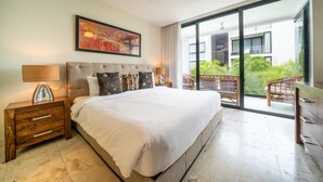A bedroom with a large bed, a nightstand, a lamp, and a view of a balcony with outdoor furniture. - ANAH - Central Condo - 2 Bedrooms (Playa del Carmen)