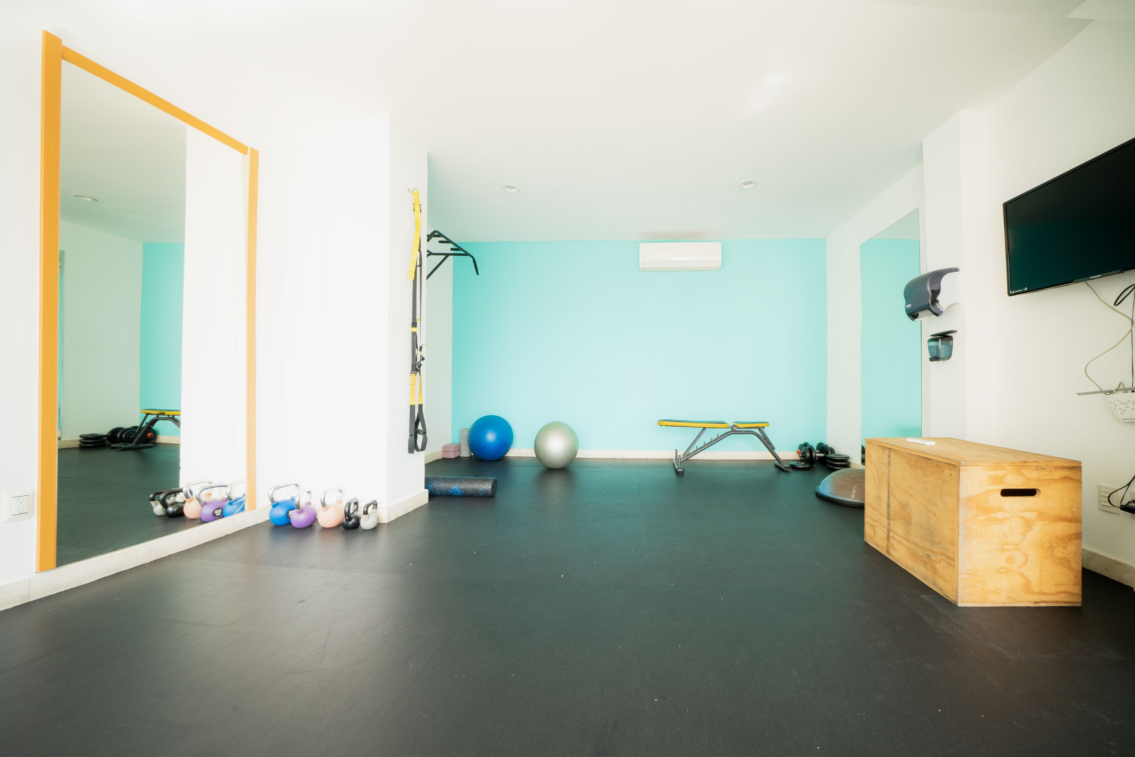 A gym with exercise equipment, a mirror, and a television on the wall.