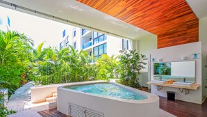 A modern indoor pool area with a wooden ceiling, surrounded by lush greenery and a view of a building with large windows. - ANAH - Central Condo - 2 Bedrooms (Playa del Carmen)