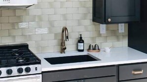 A kitchen with dark cabinets, a white stove, a sink with a gold faucet, and a pendant light. - Ulysses Suites, Suite 302 (Galena)