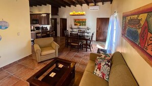 A spacious living area with a sofa, a coffee table, and a dining table set for four. A ceiling fan and a chandelier are visible. - Sueño Escondido-West Bay Beach (West Bay)