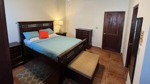 A bedroom with a bed, nightstands, a bench, a ceiling fan, and a door. - Sueño Escondido-West Bay Beach (West Bay)