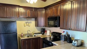 A kitchen with dark wooden cabinets, a black refrigerator, a microwave, a stove, and a toaster. - Sueño Escondido-West Bay Beach (West Bay)