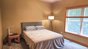 Un dormitorio con cama, lámpara de noche y ventana con persianas.