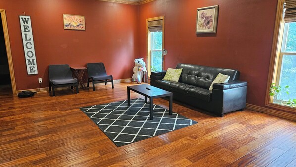 Una habitación con un sofá de cuero negro, dos sillones, una mesa de centro y un cartel de bienvenida.