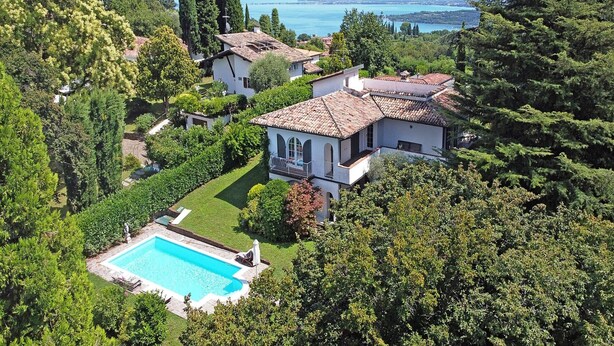 Une grande maison avec une piscine, entourée d’une végétation luxuriante et offrant une vue sur un lac.