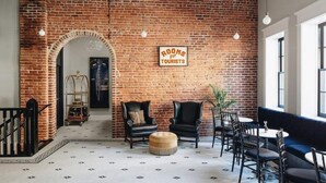 A cozy lounge area with brick walls, leather chairs, a sofa, and a sign indicating rooms for tourists. - Ulysses Suites, Suite 303 (Galena)