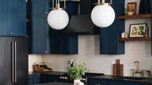 A modern kitchen with dark blue cabinets, a central island with stools, and pendant lighting. - Ulysses Suites, Suite 303 (Galena)