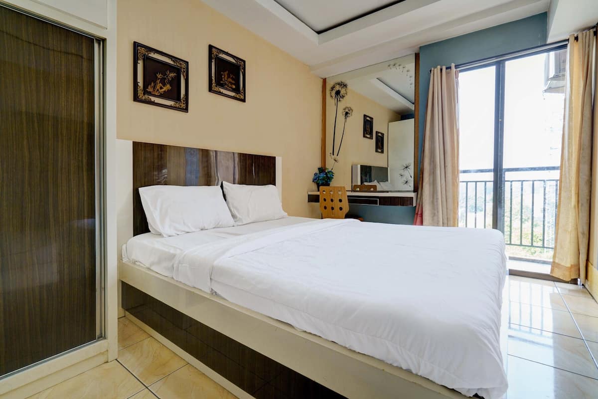 A neatly made bed with white linens, a wooden headboard, and a nightstand with a vase of flowers.