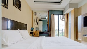 A hotel room with a large bed, a wooden headboard, a desk with a chair, a television, and a balcony with curtains. - OYO Life 93310 Apartemen Tamansari Panoramic By Santuy 2 (Bandung)