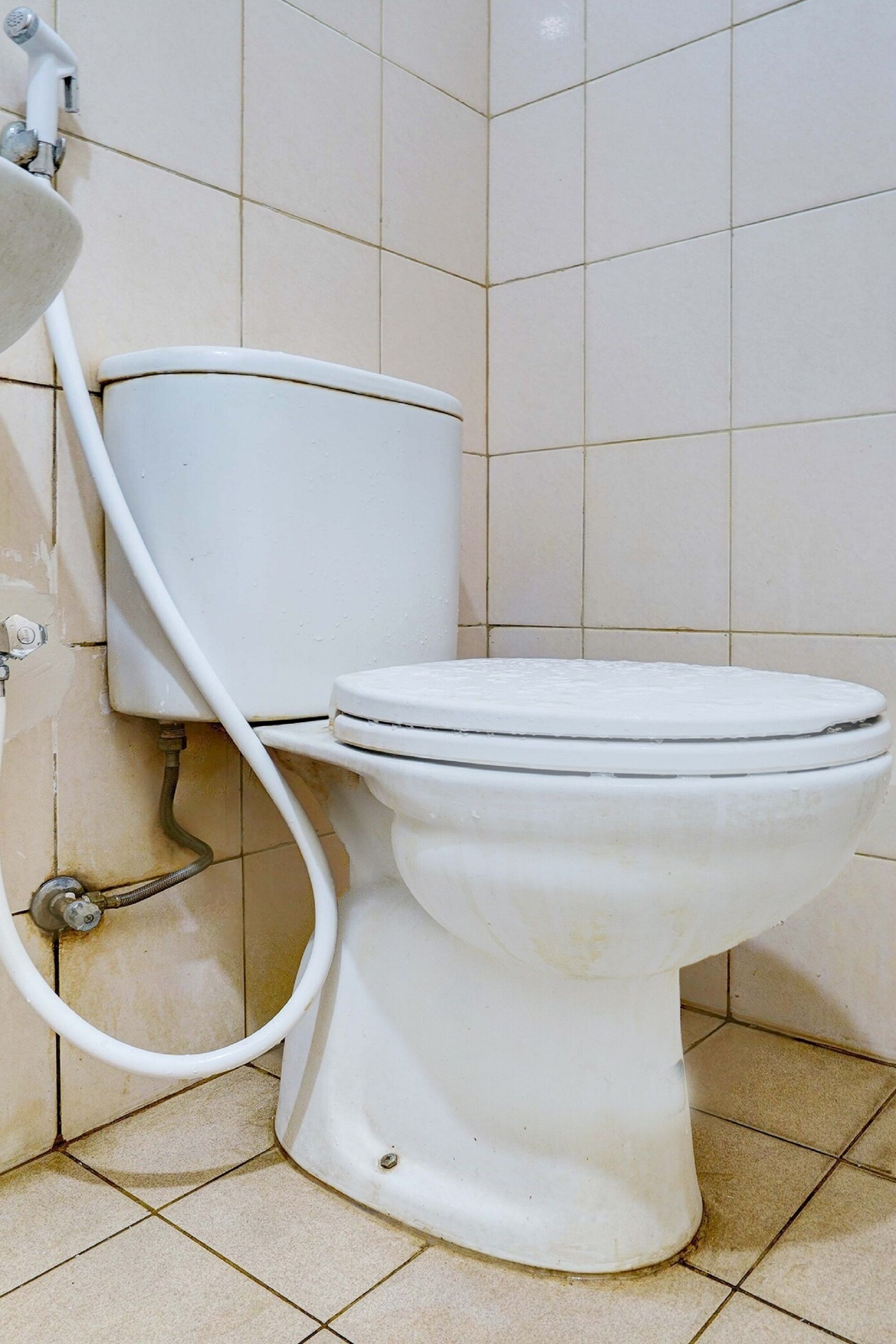 A white toilet with a tank and a seat, connected to a wall-mounted pipe.
