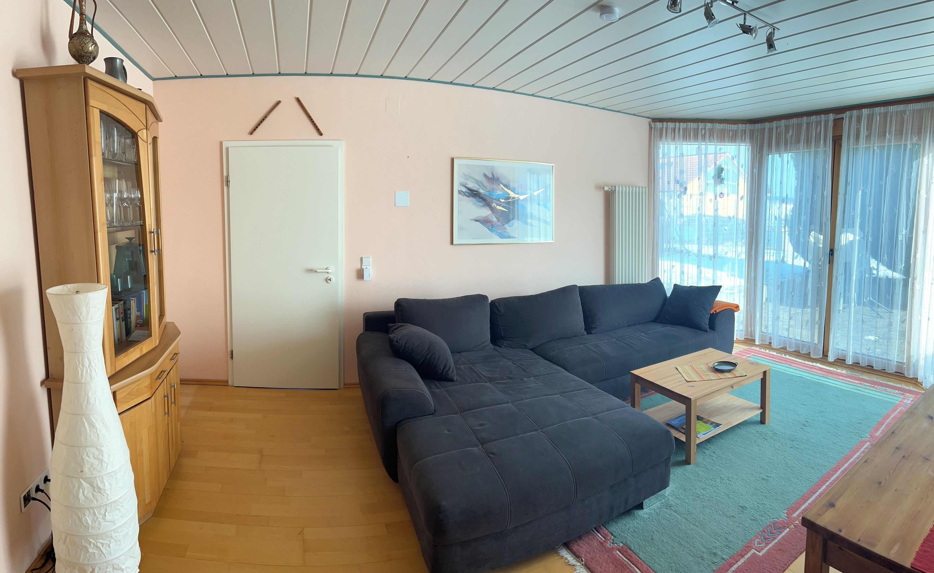 Un salón con un sofá de color oscuro, una mesa de centro de madera y un mueble con puertas de vidrio.