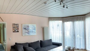 Una sala de estar con un sofá seccional gris oscuro, una mesa de centro de madera y un ventanal con cortinas de gasa.