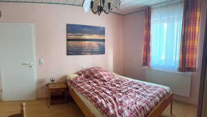 Un dormitorio con cama, mesita de noche, un cuadro, ventana con cortinas y un radiador.