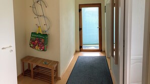 Un pasillo con un banco de madera, un perchero con un bolso y una puerta que da a una habitación con ventana.