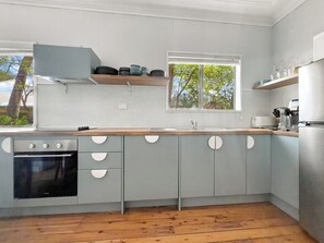 A modern kitchen with grey cabinets, a wooden countertop, a built-in oven, and a window with a view of trees. - Pearl Beach House - 2 min to sand & sea - 2 semis (Pearl Beach)