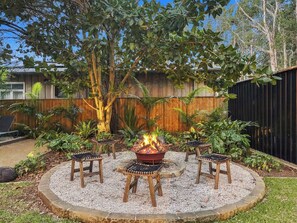 A circular outdoor seating area with a fire pit surrounded by four wooden stools.