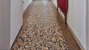 Un couloir avec un sol à motifs, un luminaire au plafond, une porte avec un rideau rouge et un tableau encadré accroché au mur.