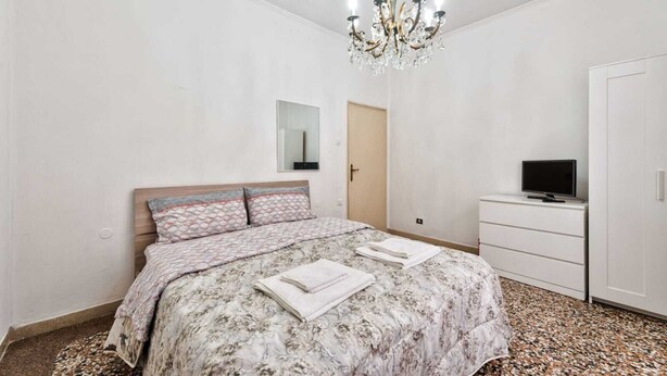 Une chambre à coucher avec un lit, un téléviseur posé sur une commode et un lustre.